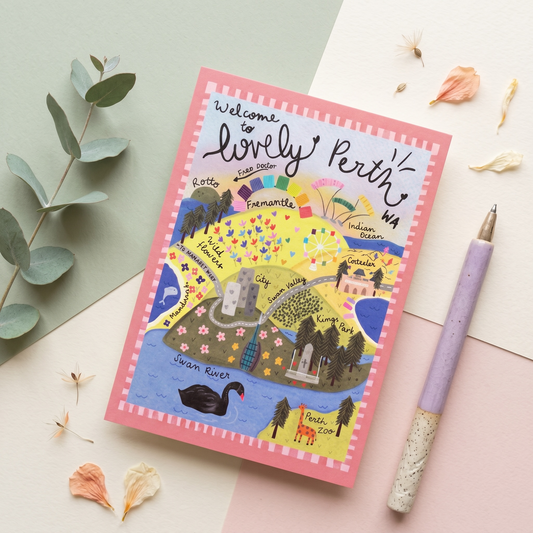 A square illustrated notebook or card titled 'Welcome to lovely Perth, WA' lies on a pastel flat-lay surface with a lavender pen beside it and eucalyptus leaves and dried petals around it. The cover shows a colorful city map with labels, trees, buildings, and a black swan.